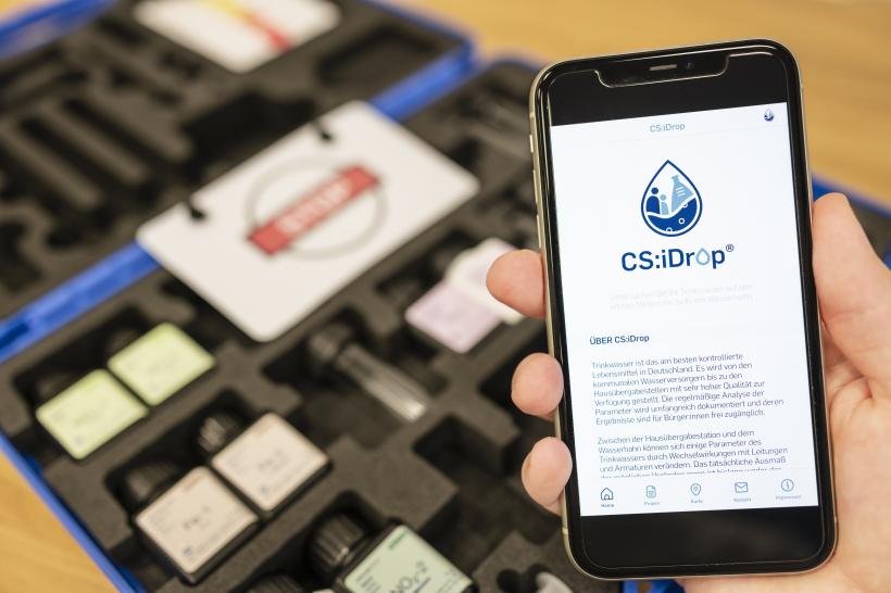 Im Hintergrund CS:iDrop-Waterbox; im Vordergrund Handy mit geöffneter CS:iDrop-App.