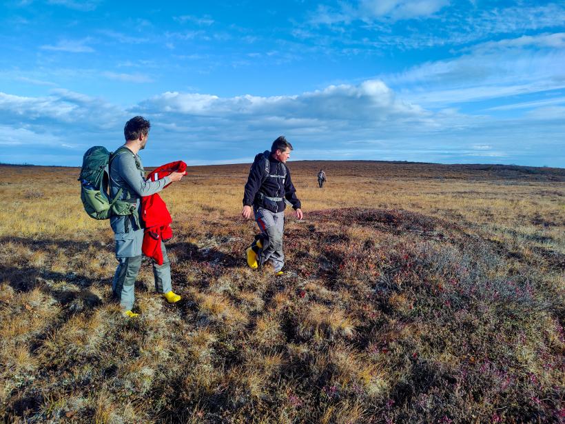 Drei Personen gehen durch eine Tundra-Landschaft.
